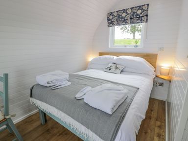 A bedroom with a bed with white bedding a gray blanket and folded robes on top at Laird Lodge 2 in Lochmaben