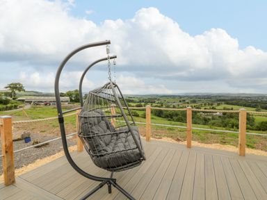 A hanging chair with cushions on a wooden deck overlooking fields and hills at Laird Lodge 2 in Lochmaben