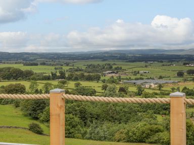 A countryside view with fields trees and farm buildings behind a rope fence at Laird Lodge 2 in Lochmaben