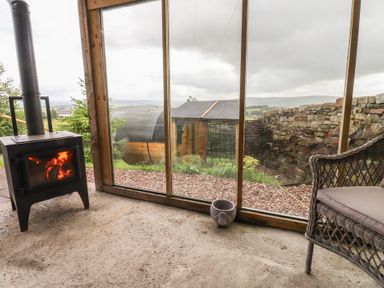 A conservatory with a wood stove and chair at The Herdsman Luxury Shepherds Hut Barnoldswick