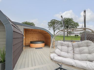 An outdoor area with a cushioned hanging chair and a covered hot tub at Laird Lodge 3 in Lochmaben