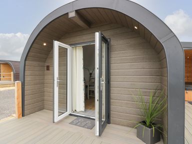 The entrance of a pod-style building with double glass doors open to the inside with a plant in a square pot on the right at Laird Lodge 3 in Lochmaben