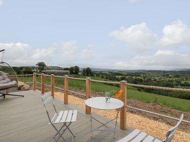 A patio with two white chairs and a small round table with a glass and flower overlooking a green landscape at Laird Lodge 3 in Lochmaben