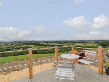 An outdoor patio with a small white table and two white chairs overlooking green fields at Laird Lodge 3 in Lochmaben