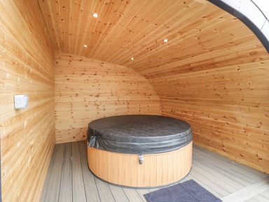 An indoor wooden room with a round covered hot tub and a small mat on the floor at Laird Lodge 3 in Lochmaben