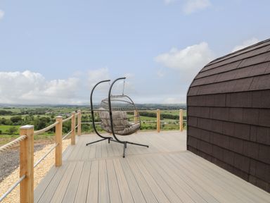 An outdoor deck with a hanging chair and a railing overlooking green fields at Laird Lodge 3 in Lochmaben
