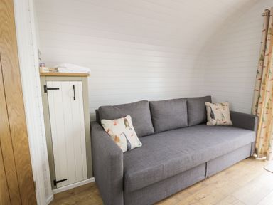 A gray sofa with patterned pillows next to a small cabinet with towels on top in a room with white wooden walls and wood flooring at Laird Lodge 4 in Lochmaben