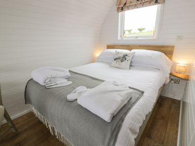 A bedroom with a double bed white linens a gray throw blanket robes and slippers on the bed with a window above and wooden floors at Laird Lodge 4 Lochmaben