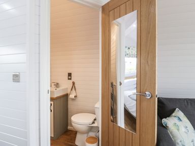 A bathroom with a toilet and sink visible through a wooden door with a mirror at Laird Lodge 4 Lochmaben