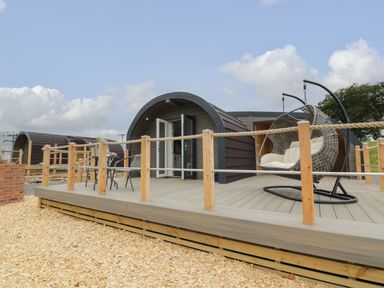 An outdoor wooden deck with a hanging chair and a table with chairs outside a curved wooden cabin at Laird Lodge 4 in Lochmaben