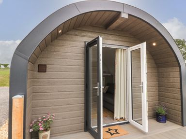 The entrance of a curved wooden structure with open glass doors and flower pots on each side at Laird Lodge 4 in Lochmaben