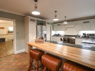 A kitchen with an island counter and bar stools and white cabinets at Tan Yr Allt in Dolanog near Meifod Powys