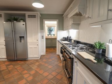 A kitchen with a stainless steel refrigerator a stove with multiple burners and ovens a black countertop with a cutting board and a potted plant and a doorway leading to a small area with a sink Tan Yr Allt in Dolanog near Meifod Powys