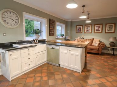 A kitchen area with white cabinets black countertops a dishwasher a sofa with pillows wall art and hanging lights at Tan Yr Allt in Dolanog near Meifod Powys