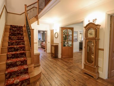 A hallway with wooden flooring a staircase with a patterned runner and a grandfather clock at Tan Yr Allt in Dolanog near Meifod Powys