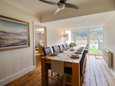A dining room with a long wooden table set for a meal and large windows showing an outdoor view at Tan Yr Allt in Dolanog near Meifod Powys