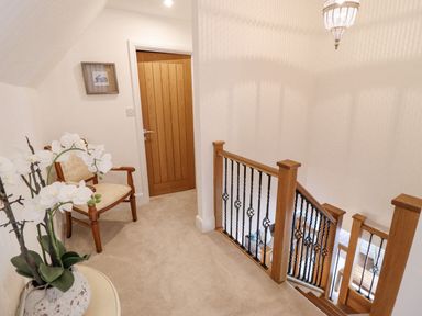 A staircase landing with wooden railing a wooden door a wooden chair and a potted plant at Tan Yr Allt in Dolanog near Meifod Powys