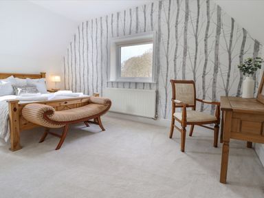 A bedroom with a wooden bed a bench at the foot of the bed a wooden chair and a wooden dressing table with a vase of flowers at Tan Yr Allt Dolanog near Meifod Powys