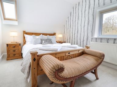 A bedroom with a wooden bed pillows bedside tables lamps bench and a window at Tan Yr Allt in Dolanog near Meifod Powys