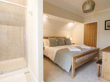 A bedroom with a wooden bed with gray pillows and folded towels and an adjacent shower cubicle at Tan Yr Allt in Dolanog near Meifod Powys