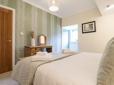 A bedroom with a bed with folded towels on a grey quilt and a wooden dressing table against a patterned wall at Tan Yr Allt in Dolanog near Meifod Powys