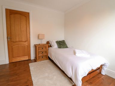 A bedroom with a single bed a wooden bedside table with a lamp a wooden door and a white rug at Tan Yr Allt in Dolanog near Meifod Powys