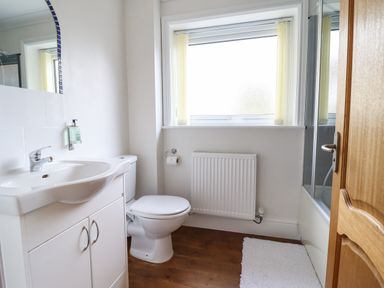 A bathroom with a sink cabinet toilet radiator and a bath with glass screen at Tan Yr Allt in Dolanog near Meifod Powys
