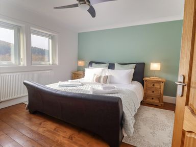 A bedroom with a black leather bed white bedding wooden bedside tables with lamps and two windows at Tan Yr Allt in Dolanog near Meifod Powys