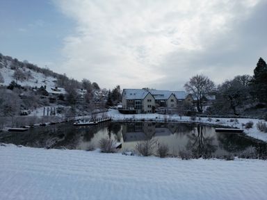 A snowy landscape with houses near a pond reflecting the buildings at Tan Yr Allt in Dolanog near Meifod Powys