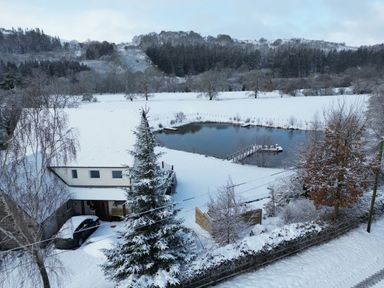 A snowy landscape with a house near a pond surrounded by trees at Tan Yr Allt in Dolanog near Meifod Powys
