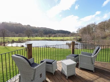 A deck with two cushioned chairs two footstools and a small table overlooking a pond and grassy field at Tan Yr Allt in Dolanog near Meifod Powys