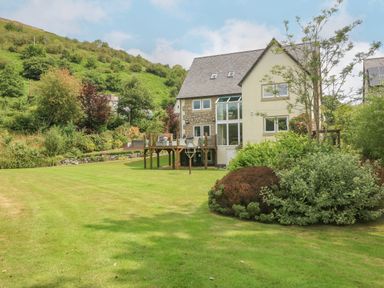 A house with a wooden deck overlooking a large lawn and garden on a hillside at Tan Yr Allt in Dolanog near Meifod Powys