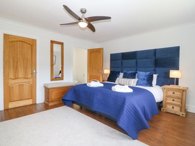 A bedroom with a blue bedspread and pillows a ceiling fan and wooden doors at Tan Yr Allt in Dolanog near Meifod Powys