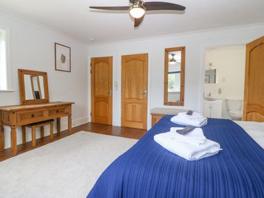 A bedroom with a blue bedspread and folded towels a wooden dresser with a mirror a wooden bench with a mirror above three wooden doors and an open door showing a bathroom at Tan Yr Allt in Dolanog near Meifod Powys