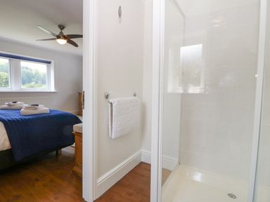 A bedroom with a bed and ceiling fan next to a bathroom with a shower and towel at Tan Yr Allt in Dolanog near Meifod Powys