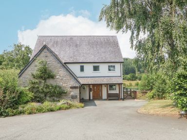 A two story house with stone and white walls a sloped roof and a driveway with surrounding greenery at Tan Yr Allt in Dolanog near Meifod Powys