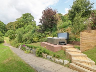 An outdoor hot tub on a wooden platform with steps leading up to it surrounded by greenery and trees at Tan Yr Allt in Dolanog near Meifod Powys