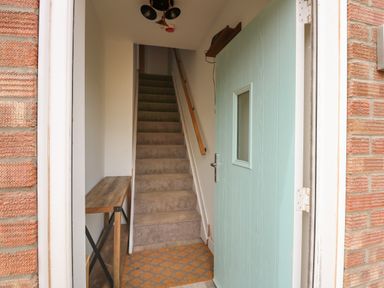 An entrance hallway with carpeted stairs a wooden bench and a light blue front door at Jolly Sailors Retreat - Wells next the Sea in Wells-Next-The-Sea