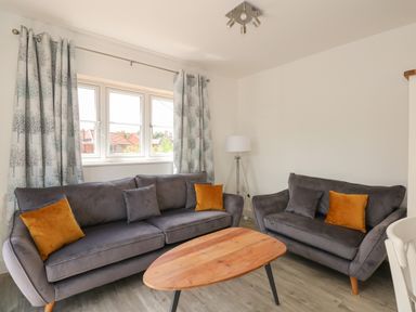 A living room with two grey sofas with orange and grey cushions a wooden coffee table and patterned curtains at Jolly Sailors Retreat - Wells next the Sea