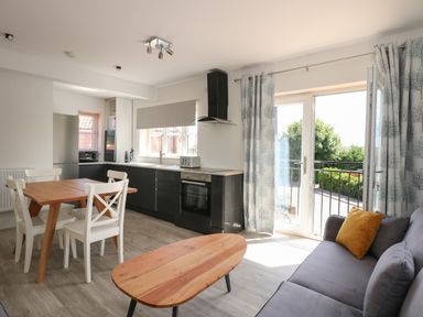 A kitchen and dining area with a wooden table and white chairs next to a gray sofa and coffee table at Jolly Sailors Retreat - Wells next the Sea in Wells-Next-The-Sea