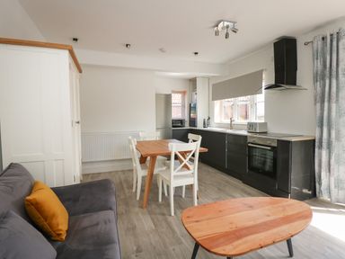 A kitchen and dining area with a wooden table and white chairs next to black cabinets and a sofa at Jolly Sailors Retreat - Wells next the Sea in Wells-Next-The-Sea