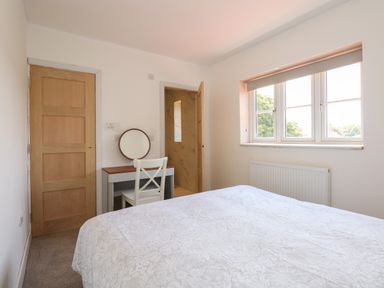A bedroom with a bed a window a dressing table with a round mirror and a chair at Jolly Sailors Retreat in Wells Next The Sea