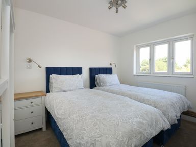 A bedroom with two single beds with blue headboards a bedside table and a window at Jolly Sailors Retreat - Wells next the Sea in Wells-Next-The-Sea