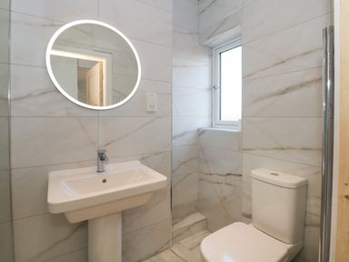A bathroom with a pedestal sink toilet and a round illuminated mirror at Jolly Sailors Retreat - Wells next the Sea in Wells-Next-The-Sea