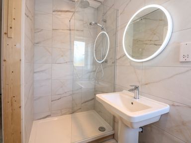 A bathroom with a shower enclosure sink and a round illuminated mirror at Jolly Sailors Retreat - Wells next the Sea in Wells-Next-The-Sea
