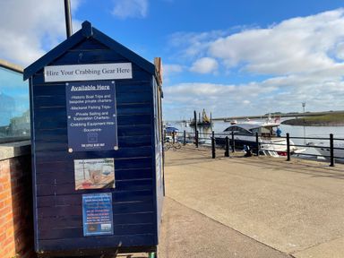 A blue hut with signs for crabbing gear hire next to a harbor with boats and railings at Jolly Sailors Retreat - Wells next the Sea in Wells-Next-The-Sea