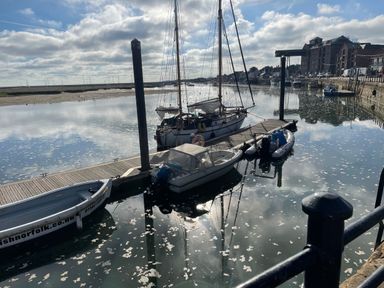 A marina with several boats docked along a wooden pier next to buildings and a railing at Jolly Sailors Retreat - Wells next the Sea in Wells-Next-The-Sea
