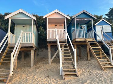 A set of wooden beach huts on stilts with stairs leading down to sand at Jolly Sailors Retreat - Wells next the Sea in Wells-Next-The-Sea
