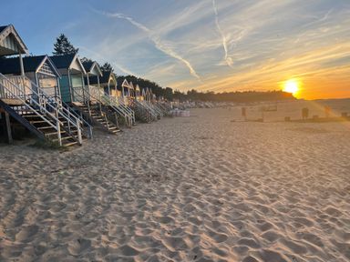 A sandy beach with rows of wooden beach huts and a sunset on the horizon at Jolly Sailors Retreat - Wells next the Sea in Wells-Next-The-Sea