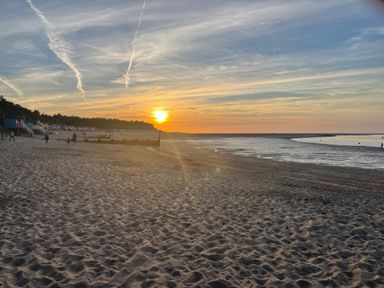 A sandy beach with people walking and sun setting over the horizon at Jolly Sailors Retreat - Wells next the Sea in Wells-Next-The-Sea